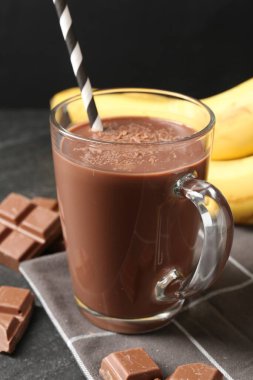 Cam bardakta lezzetli çikolatalı süt, siyah masada parçalar ve muzlar, yakın plan.