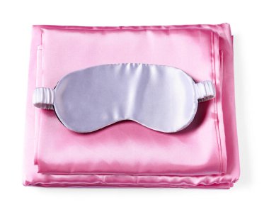 Beyaz arka planda ipek çarşaflar ve uyku maskesi, üst manzara.