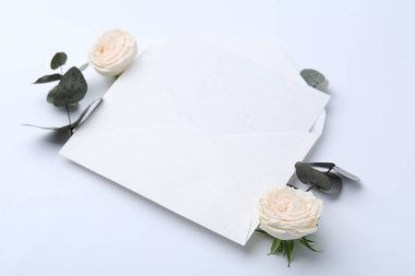 Zarfta boş tebrik kartı, okaliptüs yaprakları ve beyaz arka planda güller