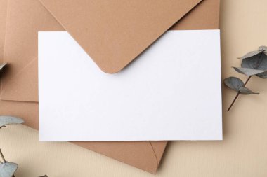 Boş tebrik kartı, zarflar ve okaliptüs yaprakları bej arka planda, düz uzanmış