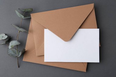 Boş tebrik kartı, zarflar ve okaliptüs yaprakları gri arka planda, düz yatıyordu.