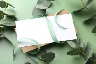 Açık yeşil zemin üzerinde boş kart, kurdele ve okaliptüs dalları, yakın plan