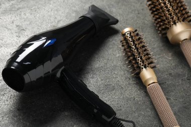 Gri desenli arka planda saç kurutma makinesi ve fırçalar, yakın plan.