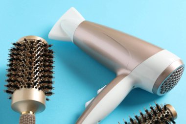 Açık mavi arkaplanda saç kurutma makinesi ve fırçalar, yakın plan.