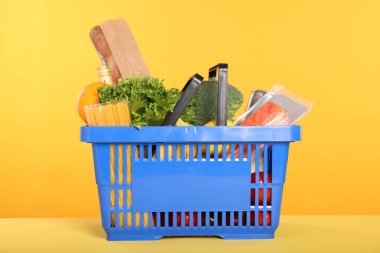 Sarı arka planda farklı gıda ürünleri olan alışveriş sepeti.