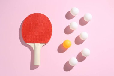 Masa tenisi raketi ve toplar pembe arka planda, düz yatıyordu.