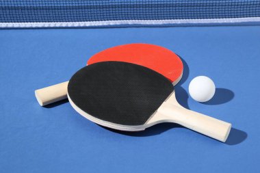 Masa tenisi raketleri, top ve ağ mavi arka planda, yakın plan
