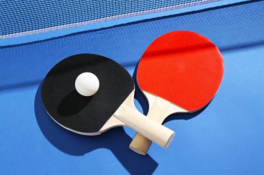 Masa tenisi raketleri, top ve ağ mavi arka planda, yakın plan