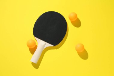 Masa tenisi raketi ve toplar sarı arka planda, üst manzara