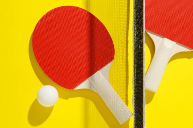 Ping pong raketleri, top ve ağ sarı arka planda, düz yatıyordu