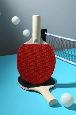 Masa tenisi raketleri, toplar ve ağ açık mavi masada.