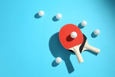 Ping pong rackets and balls on light blue background, flat lay. Space for text
