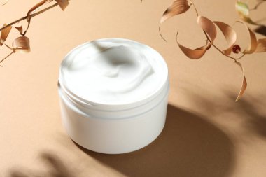 Bej arka planda bir kavanoz vücut kremi ve kuru dallar, yakın plan.