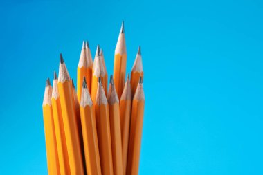 Açık mavi arka planda keskin grafit kalemler, yakın plan. Metin için boşluk