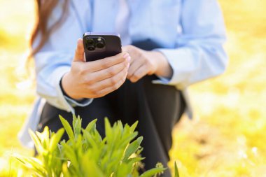 Güneşli bir günde akıllı telefondan bitki tanıma uygulaması kullanan bir kadın.