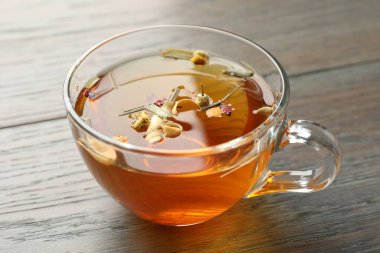 Ahşap masanın üzerinde cam bardakta Aromatik bitki çayı, yakın plan.