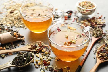 Aromatik bitki çayı ve kuru yapraklar gri masada, yakın plan.