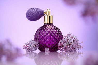 Bir şişe parfüm ve ayna yüzeyinde eflatun rengine karşı leylak çiçekleri, seçici odak