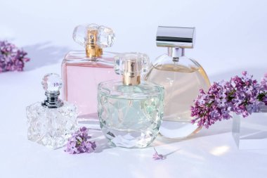 Açık gri arka planda leylak çiçekli parfüm şişeleri ve dallar, yakın plan.