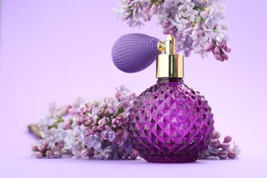 Parfüm şişesi ve mor arkaplanda leylak çiçekleri, yakın plan.