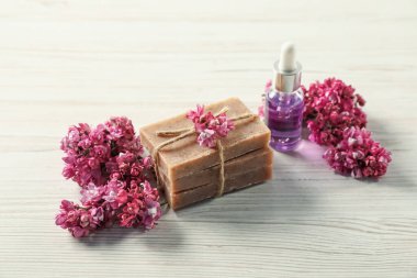 Sabun yığını, temel yağ ve leylak çiçekleri açık ahşap masada, yakın plan.