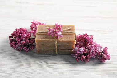 Beyaz ahşap masada sabun ve leylak çiçekleri yığını, yakın plan.