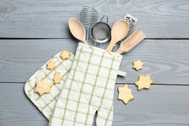 Fırın eldiveninde farklı mutfak aletleri ve açık gri ahşap masada yıldız şeklinde kurabiyeler.