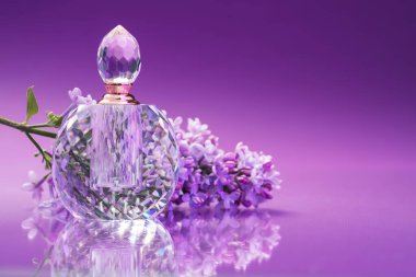 Bir şişe parfüm ve ayna yüzeyinde leylak çiçekleri olan bir dal. Renk eğilimli arka plan, yakın plan. Metin için boşluk