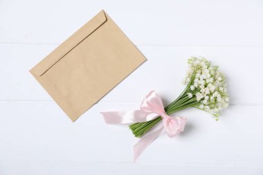 Bir buket güzel vadi zambağı çiçekleri ve beyaz ahşap arka planda bir zarf.