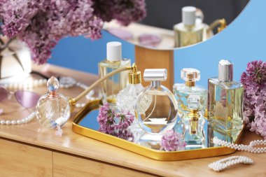 Parfümlü şişeler, eflatun çiçekleri ve tuvalet masasında aksesuarlar.