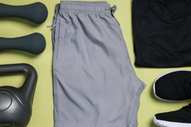 Spor kıyafetleri, spor ayakkabıları, dambıllar ve soluk zeytin arka planda kettlebell, düz uzanmış