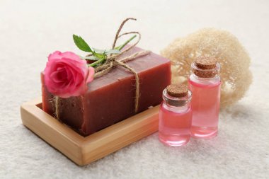 Sabun çubuğu, lif süngeri, temel yağlar ve bej masa üzerinde güzel bir gül, yakın plan.