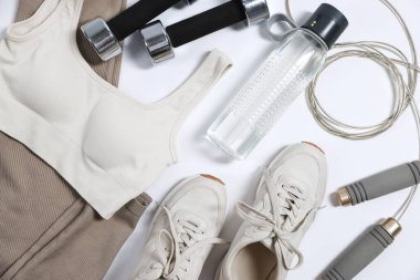 Spor kıyafetleri, spor ayakkabıları, dambıllar, atlayan ip ve su şişesi beyaz arka planda, düz yatıyordu.