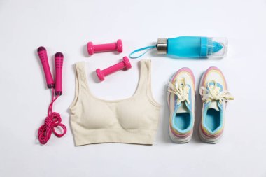 Spor kıyafetleri, dambıllar, atlama halatı ve su şişesi beyaz arka planda, düz yatıyordu.