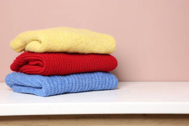 Beyaz masadaki yün kazak yığını renk arka planına karşı. Metin için boşluk