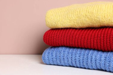 Beyaz masadaki yün kazak yığını renk arka planına karşı, yakın plan. Metin için boşluk