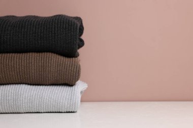 Beyaz masadaki yün kazak yığını renk arka planına karşı, yakın plan. Metin için boşluk