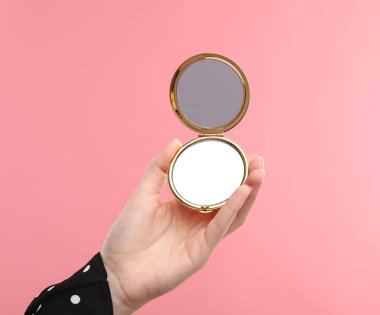 Pembe arka planda açık cep aynası tutan kadın, yakın plan.