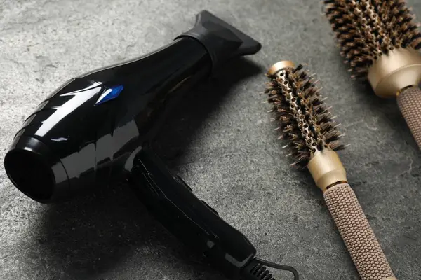 Gri desenli arka planda saç kurutma makinesi ve fırçalar, yakın plan.