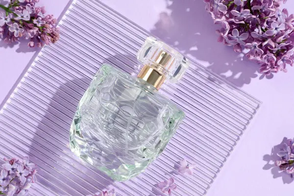 Bir şişe parfüm ve açık mor arka planda güzel leylak çiçekleri.
