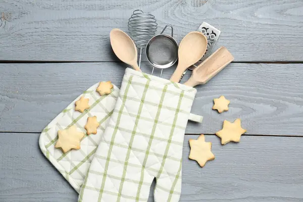 Fırın eldiveninde farklı mutfak aletleri ve açık gri ahşap masada yıldız şeklinde kurabiyeler.