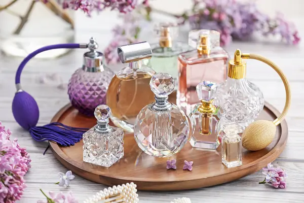 Parfüm şişeleri, aksesuarlar ve beyaz ahşap masada leylak çiçekleri, yakın plan.