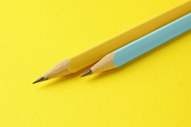 Sarı arkaplanda iki grafit kalem, yakın plan.