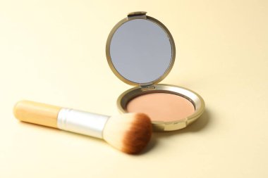 Aynalı yüz pudrasını aç ve bej arkaplanda fırçala, yakın plan