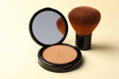 Aynalı yüz pudrasını aç ve bej arkaplanda fırçala, yakın plan