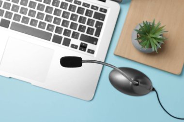 Profesyonel mikrofon, dizüstü bilgisayar, dizüstü bilgisayar ve açık mavi arka planda çiçek dekoru, düz konum