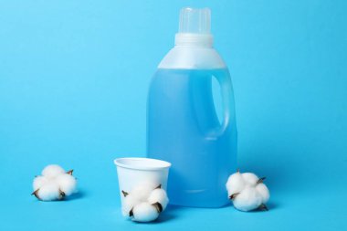 Açık mavi arkaplanda bir şişe yumuşatıcı, kep ve pamuk çiçeği.