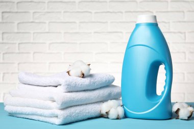 Beyaz tuğla duvara karşı açık mavi masada yumuşatıcı, havlu ve pamuk çiçekleri.