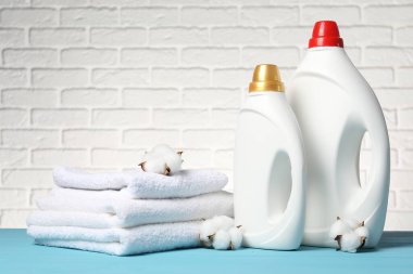 Beyaz tuğla duvara karşı açık mavi masada yumuşatıcı, havlu ve pamuk çiçekleri.