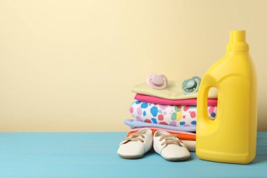 Kumaş yumuşatıcı, bebek kıyafetleri ve bej arka planda açık mavi ahşap masa üzerinde emzik. Metin için boşluk